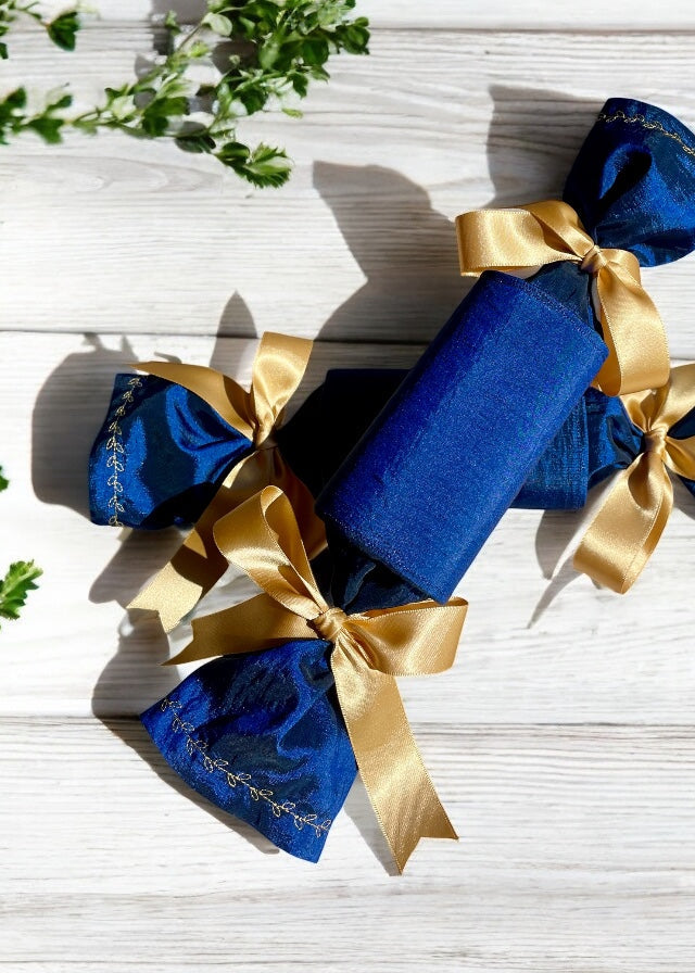 Two navy blue luxury reusable celebrations crackers with gold ribbons and gold embroidery detail on the sleeves.