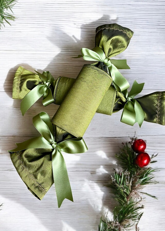 “Two Olive Green luxury Christmas crackers with olive green bows and gold embroidered edges on white table with greenery by Timeless celebrations Ireland”